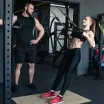 Un homme et une femme faisant des squats dans une salle de sport.
