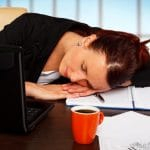 Une femme au métabolisme lent qui dort à son bureau avec une tasse de café.