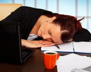 Une femme au métabolisme lent qui dort à son bureau avec une tasse de café.